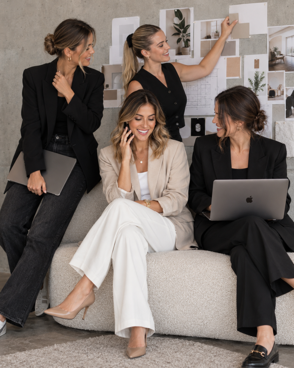 Four women sitting on a couch with laptops, and talking on their cell phones