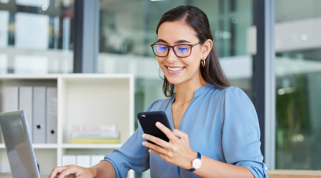 Woman sitting at a desk with a laptop and a cell phone in front of her